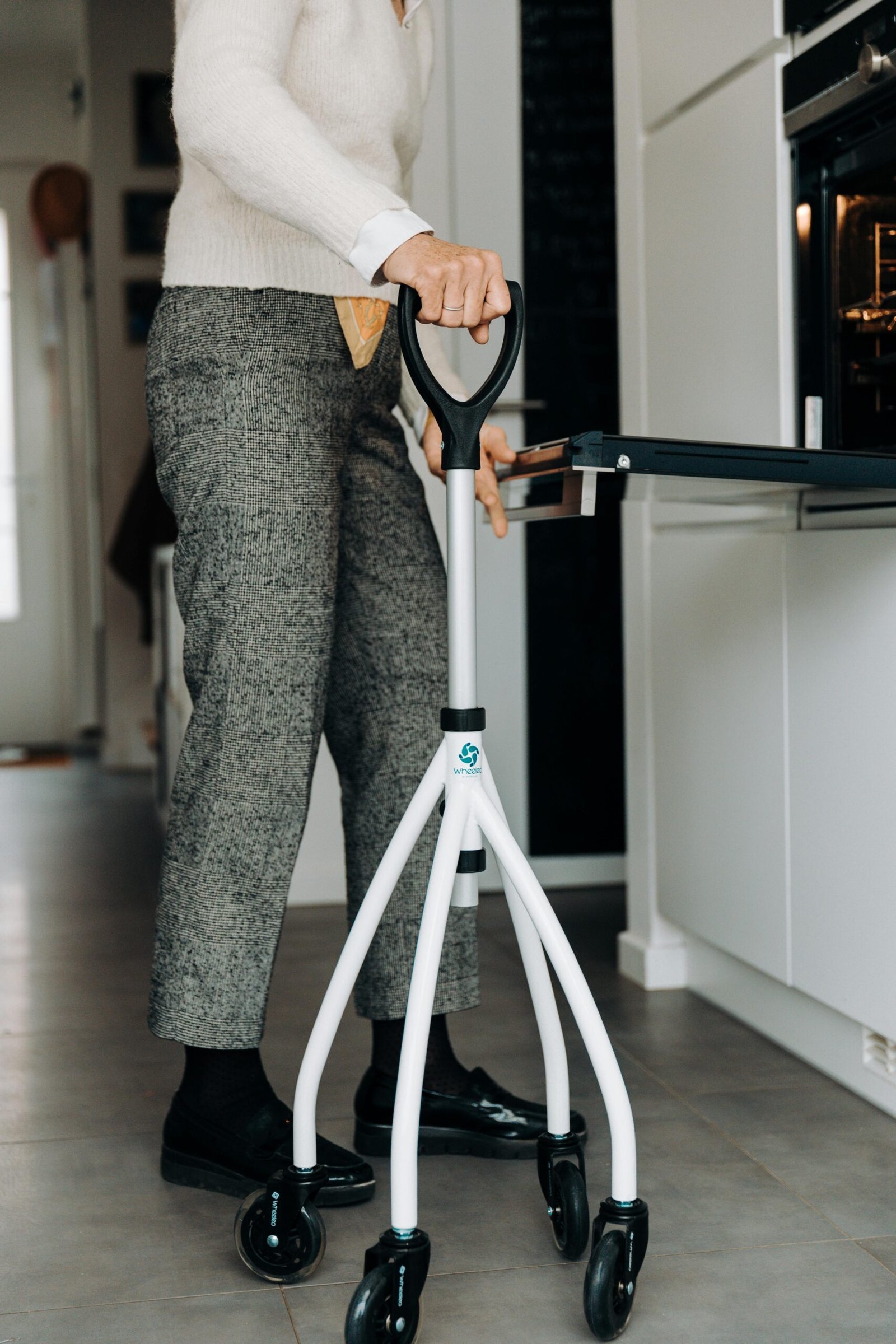 Senior adult standing with a walker in the kitchen, utilizing mobility aid for support.