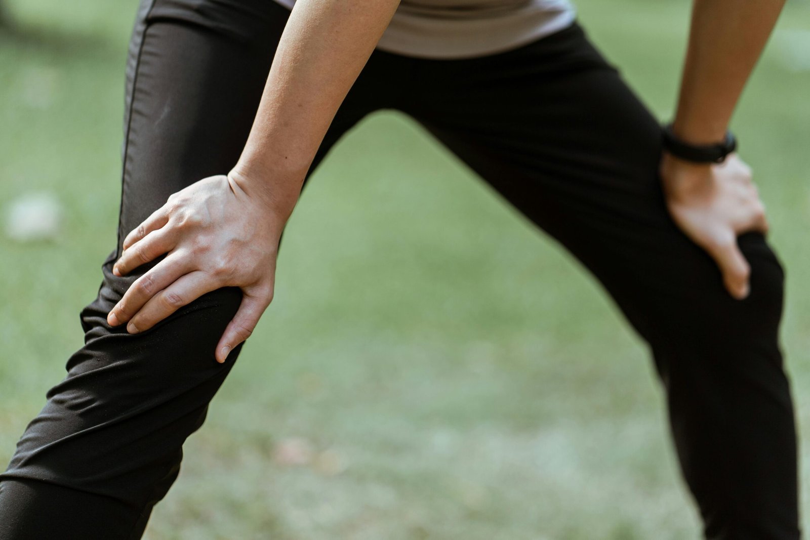 Faceless athlete resting outdoors, showcasing fitness and determination in a sunny park setting.