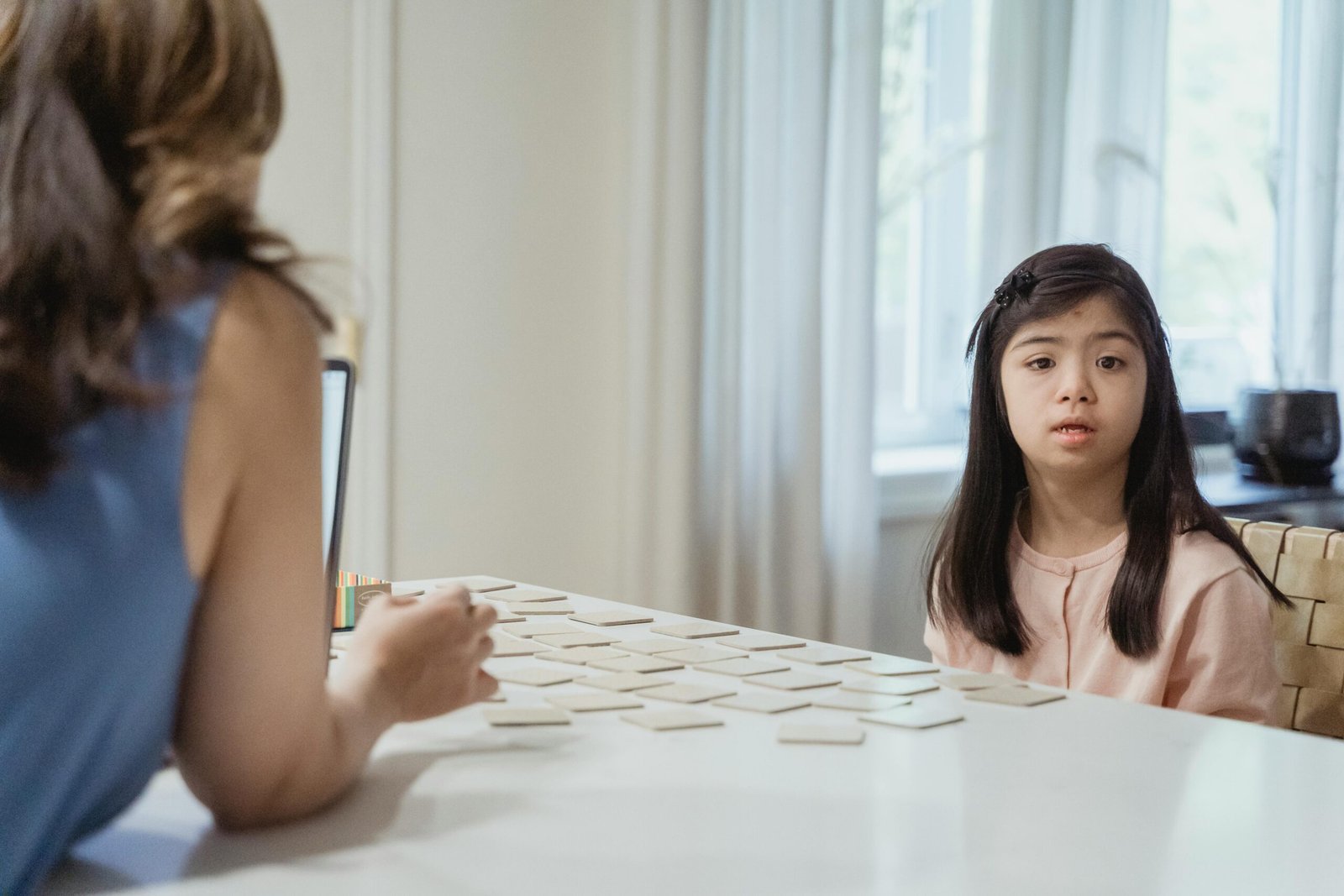 Young girl with Down Syndrome sitting at table playing card game indoors.